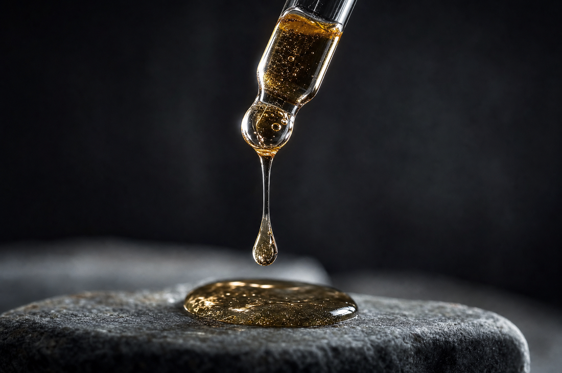 Glass dropper releasing a golden serum droplet drawing a fine thread